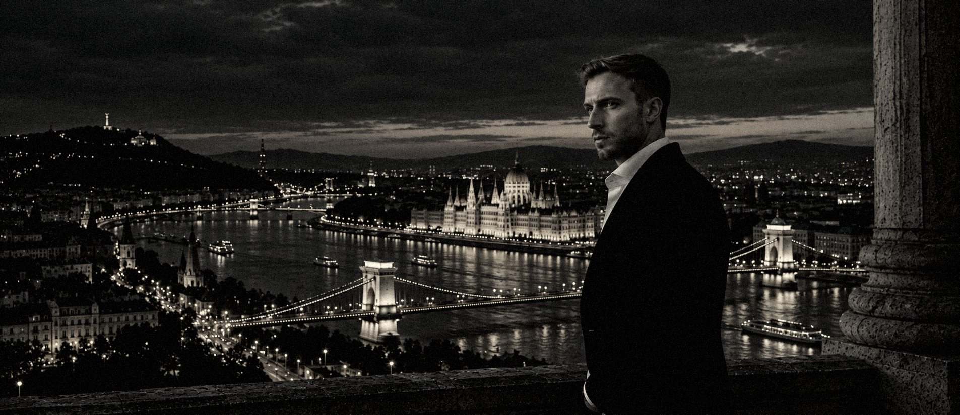Balázs Schultz on a terrace above the Danube at night, Parliament and the Chain Bridge behind